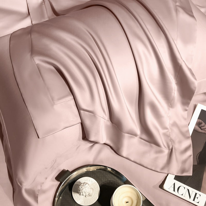 Silky blush pink Tencel Lyocell pillowcase on a bed, with candle and magazine nearby.