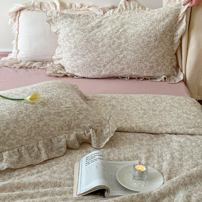 Detailed shot of the woodland cotton comforter sets, showing the texture of the muslin fabric and the ruffled pillowcases with the small rabbit print. Styled with a candle and an open book.